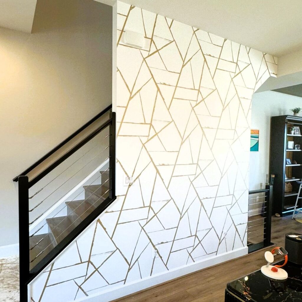 A white accent wall featuring a gold geometric line pattern situated next to a staircase with modern black railings.